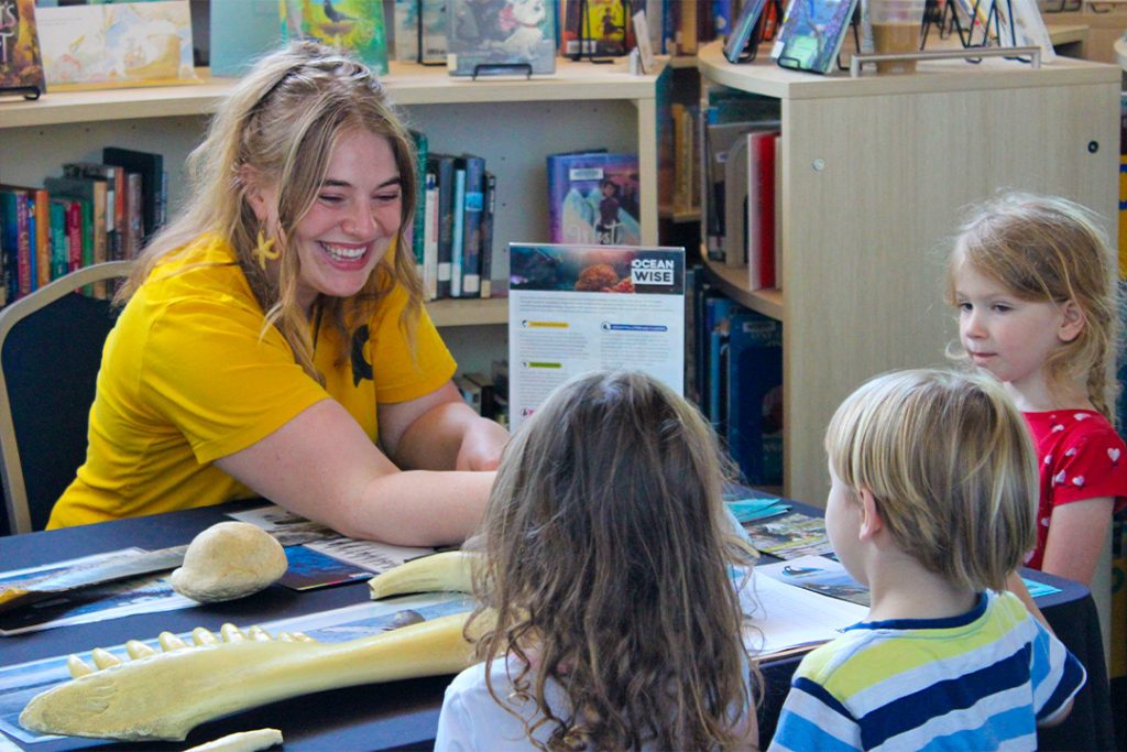 An Ocean Wise staff shows marine artifacts to a group of children at a table